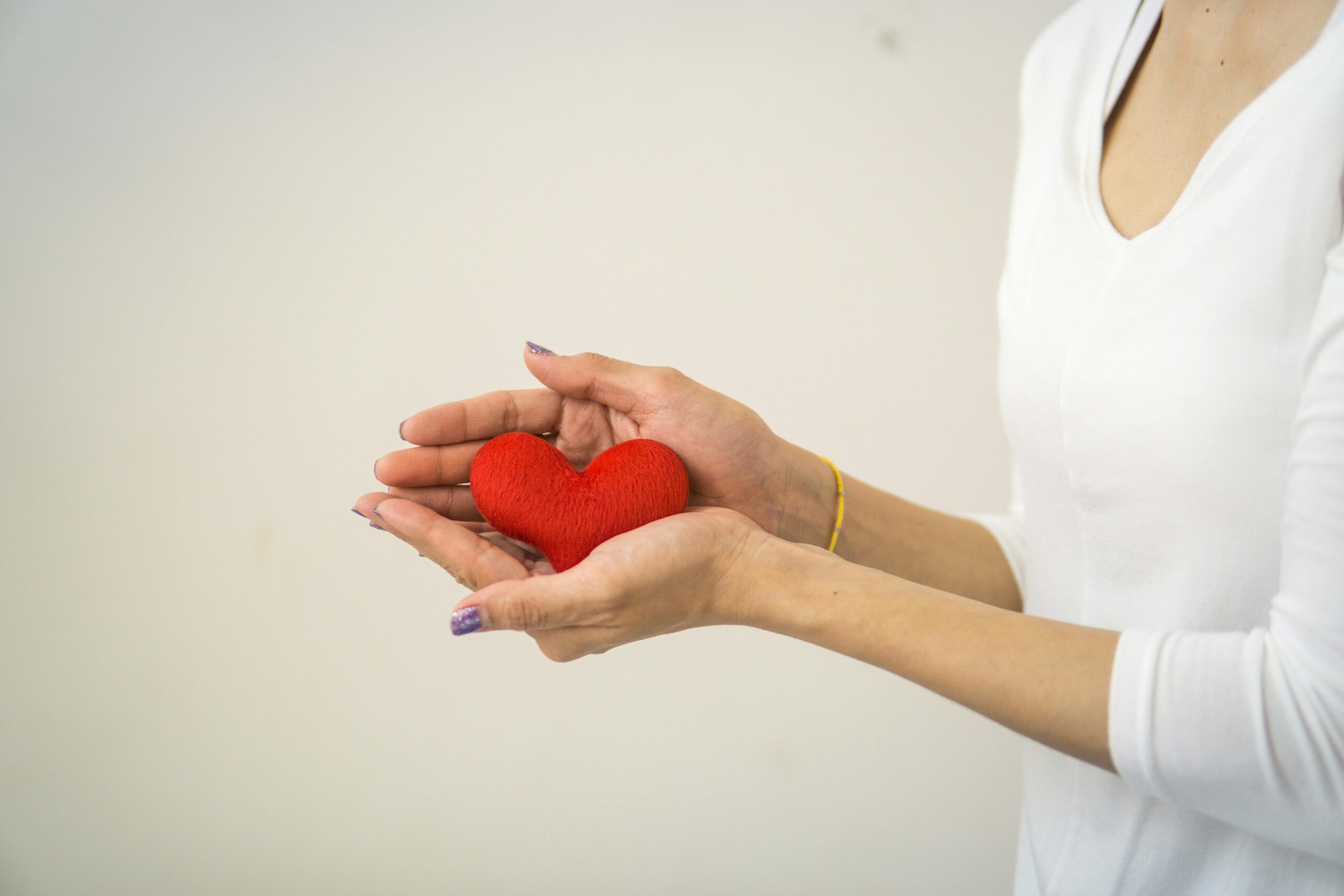 Close-up of woman's hands holding a red heart symbol, signifying love and charity.